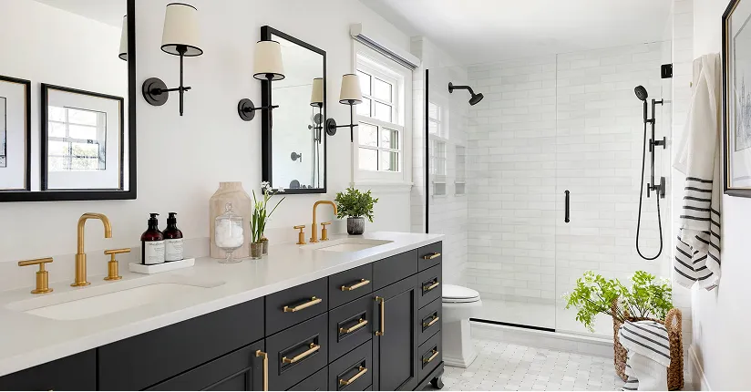 Modern bathroom with dual black vanities, gold fixtures, wall sconces, glass shower, and white tile floors.