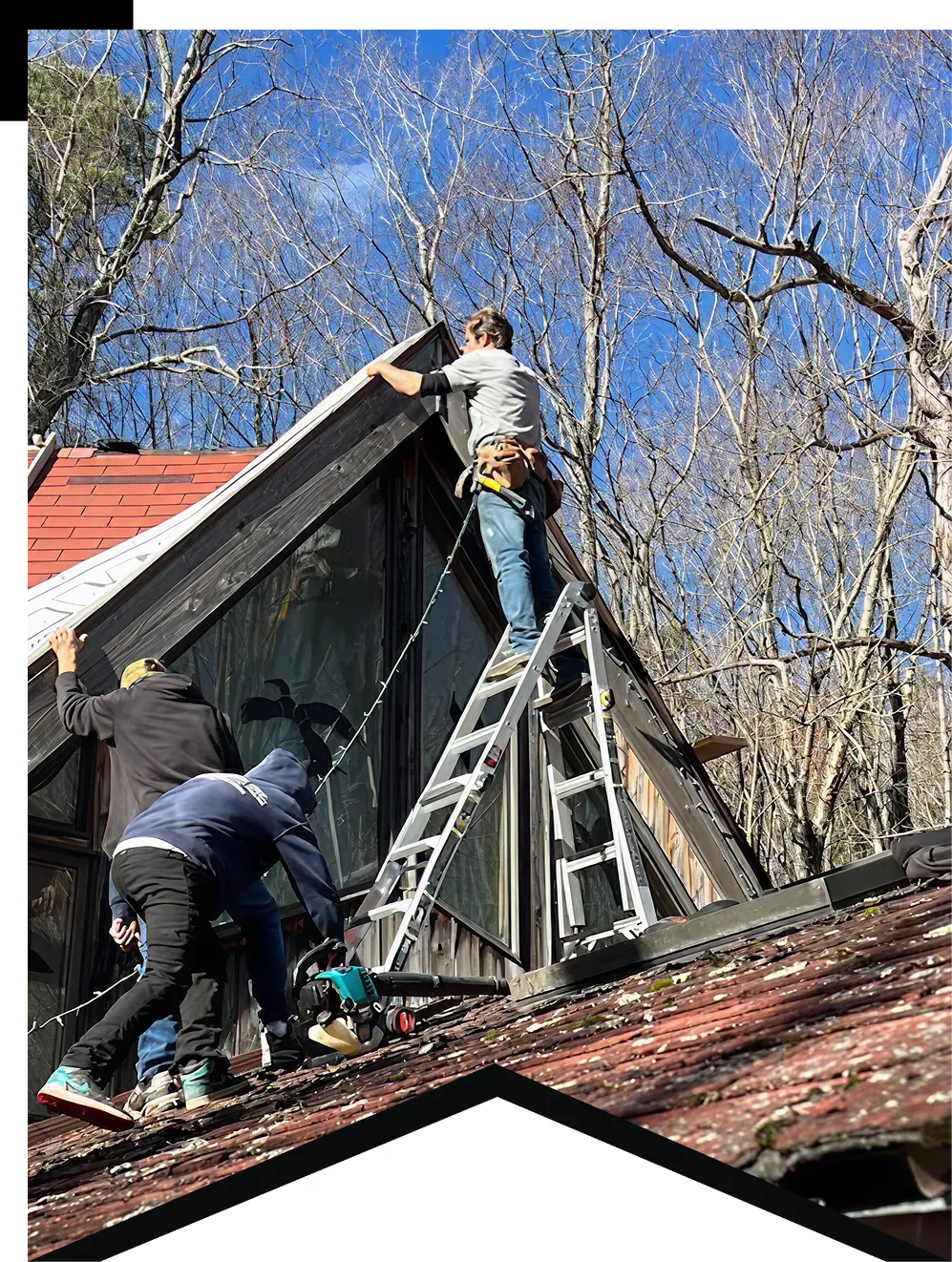 Three men working on a house roof; one on ladder fixing the triangular window frame.