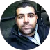 Man with short dark hair and beard wearing a dark jacket, looking at the camera indoors.