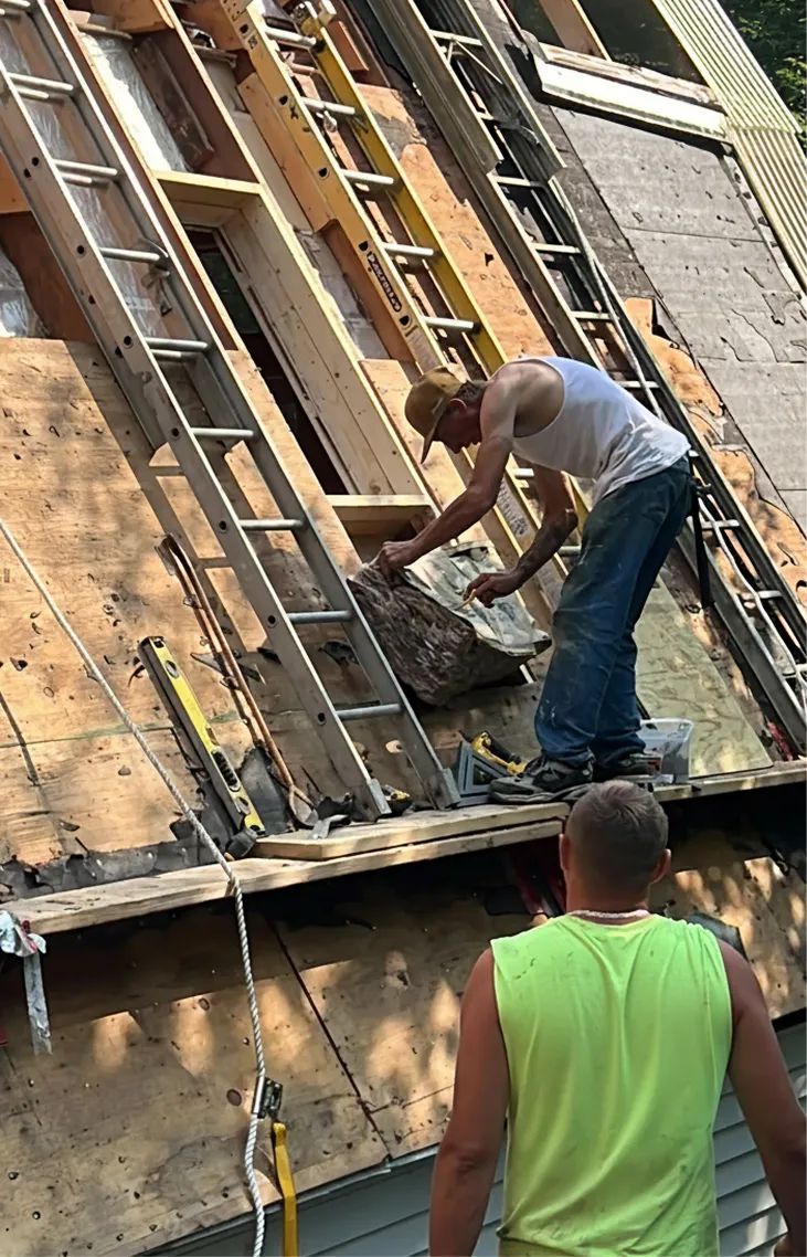 Construction workers on a steep roof with ladders installing roofing materials.