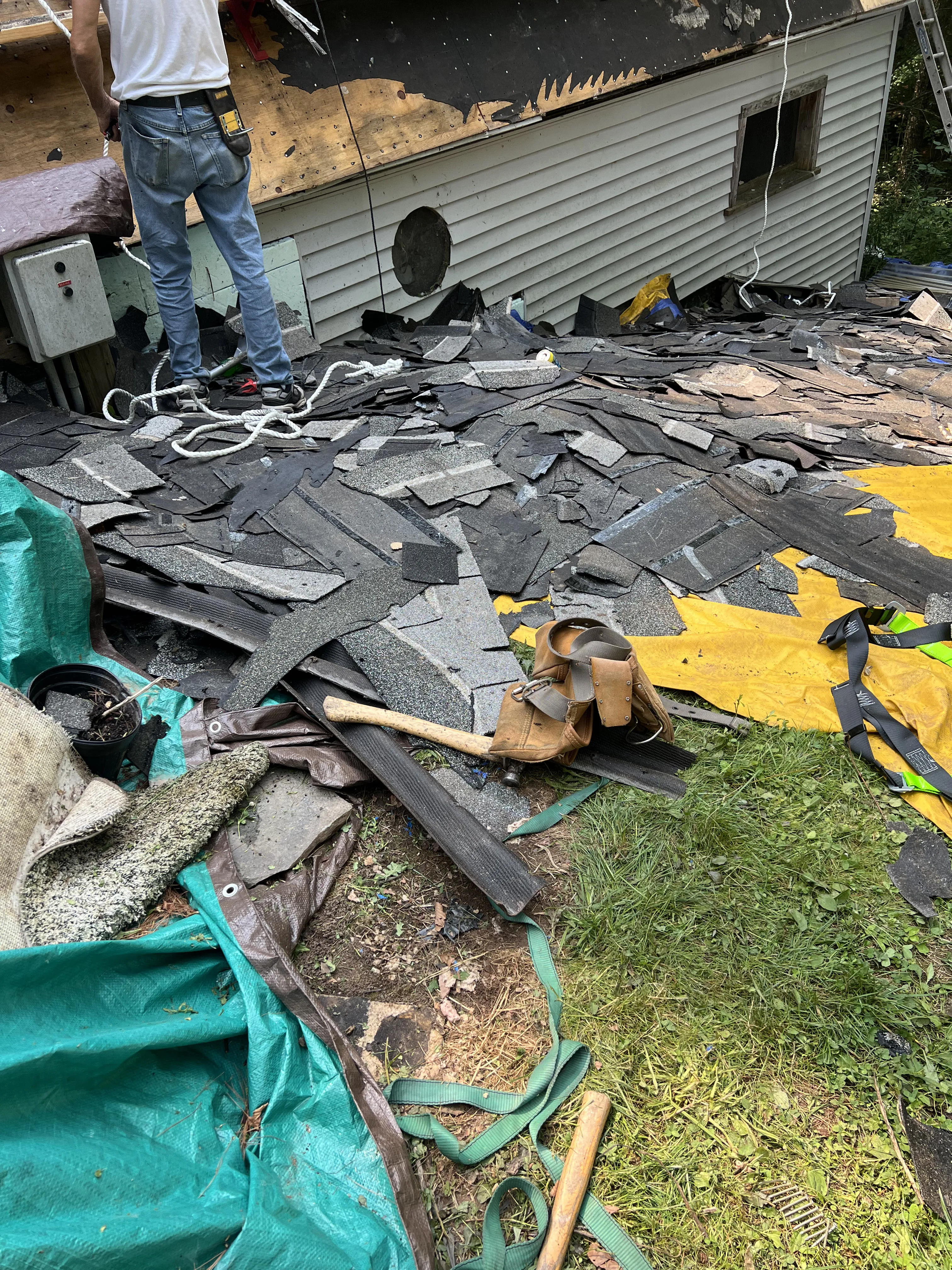 Rubble of old roof shingles on ground with tools and worker in jeans at house exterior renovation.