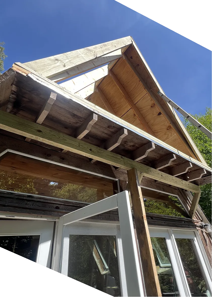 View looking up at a wooden house roof under construction with an open white door and clear blue sky.