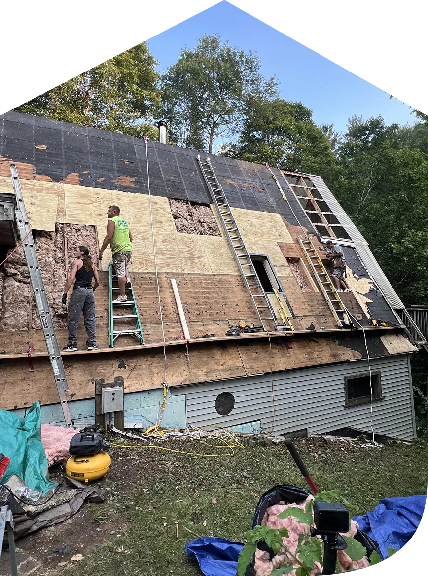 Three workers repairing and insulating a sloped roof with ladders and plywood panels during daytime.