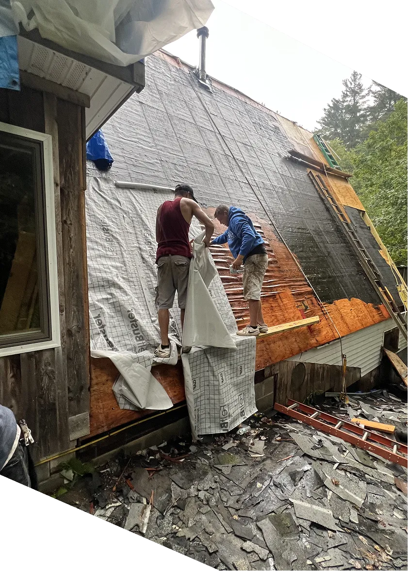 Two men working on steep roof renovation, covering wooden sheathing with waterproof underlayment.