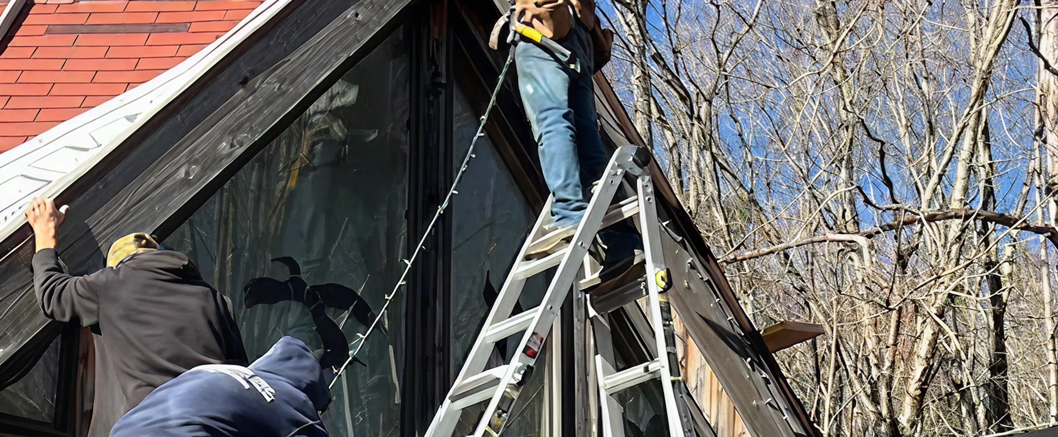 Three workers installing or repairing wooden exterior on a house using a ladder on a clear day.