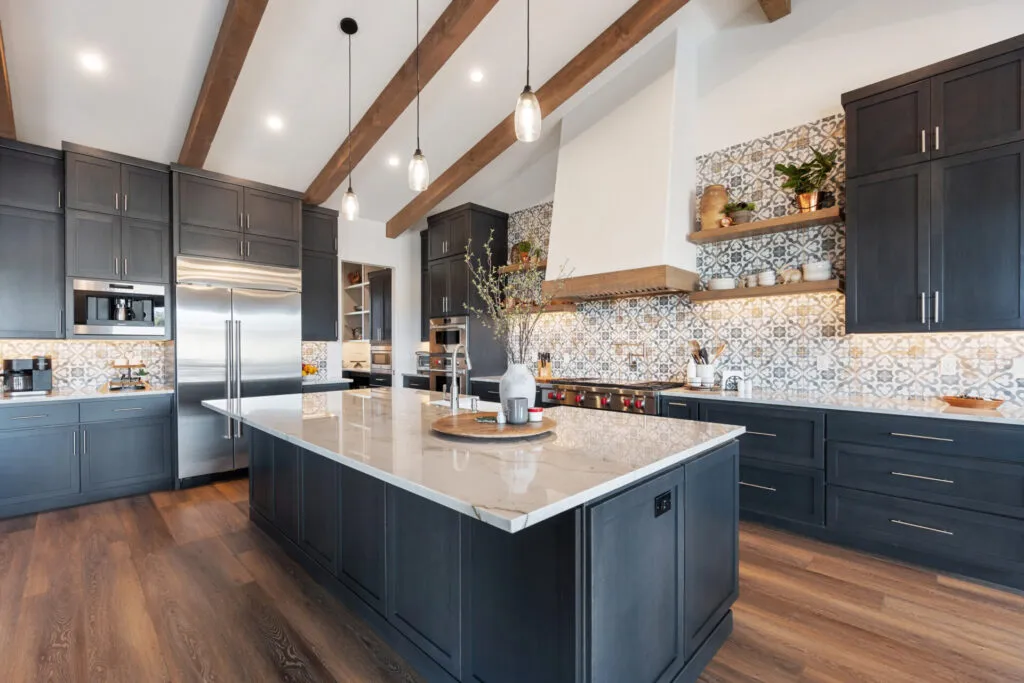 Modern kitchen with dark cabinetry, marble island, wood beams, patterned tile backsplash, and stainless steel appliances.