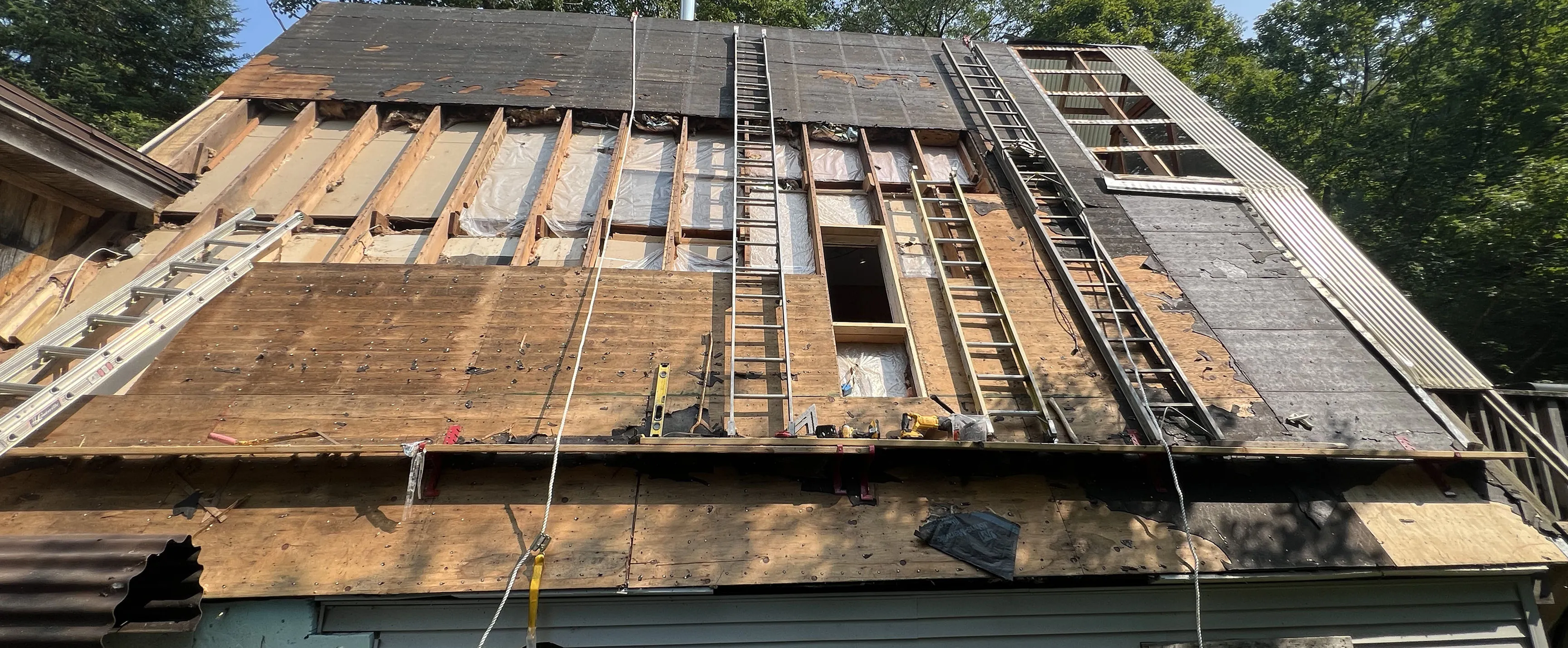 Steep roof under repair with wooden boards, ladders, ropes, and exposed insulation panels.