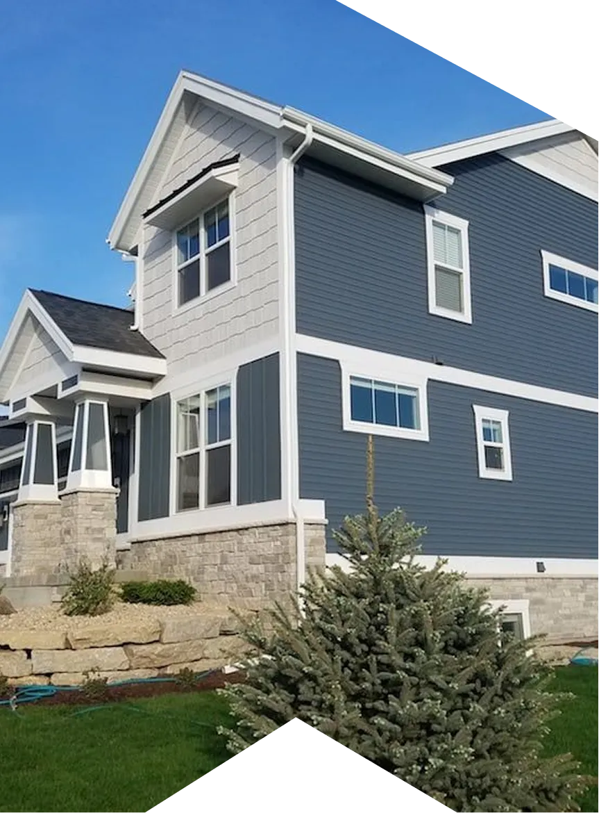 Modern two-story house with blue siding, stone foundation, and green lawn with a small pine tree.