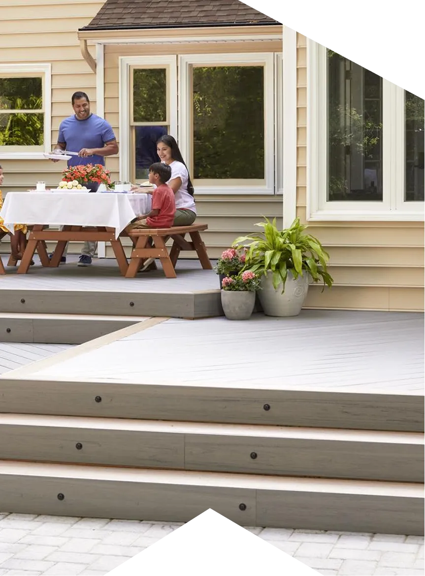 Family sitting at an outdoor picnic table with a white tablecloth on a modern wooden deck.