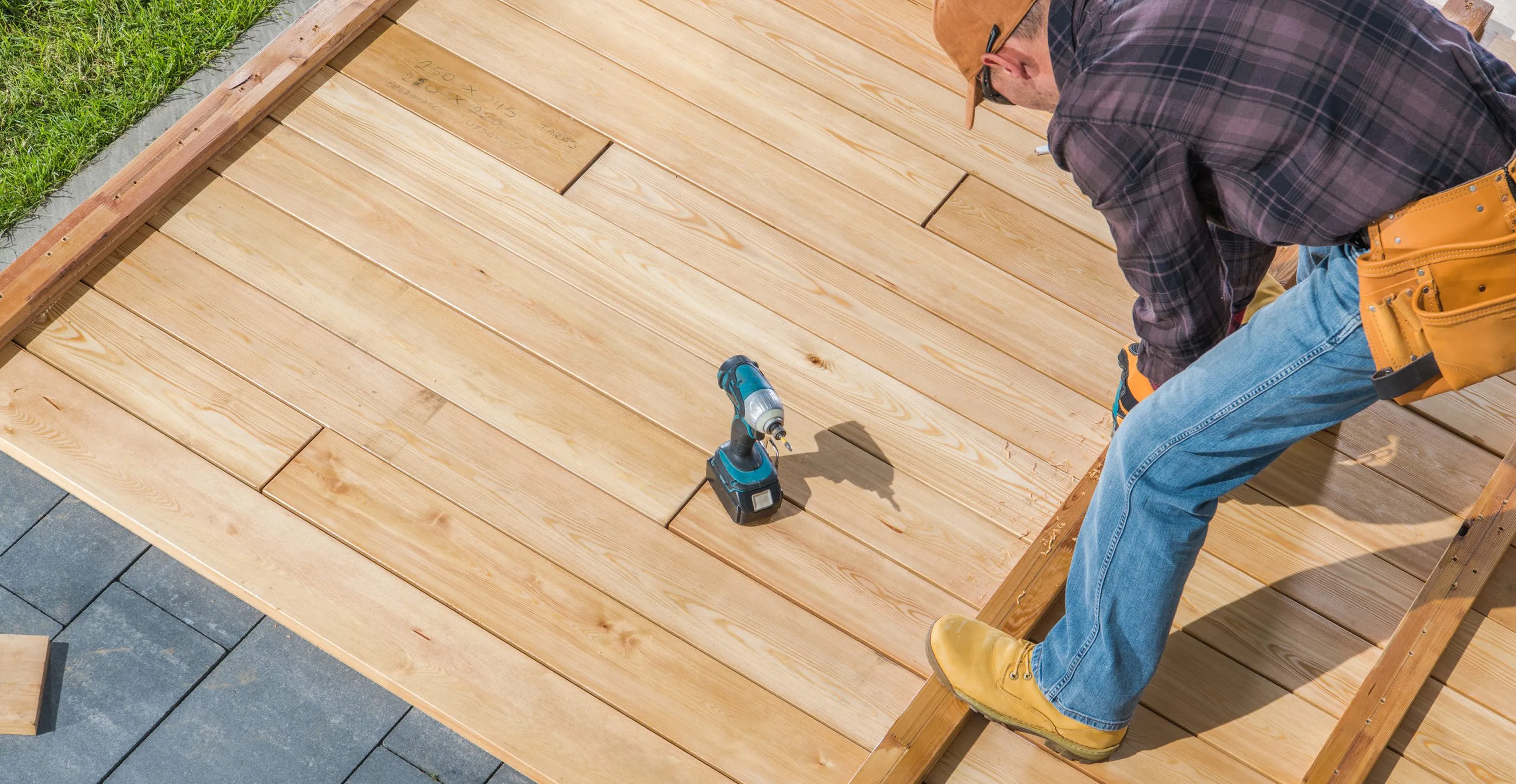 Man installing wooden deck boards using a power drill on a wooden frame outdoors.