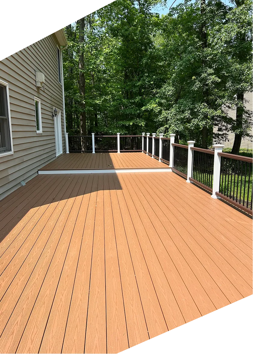 Spacious brown wooden deck attached to a house with white railing and green trees in the background.