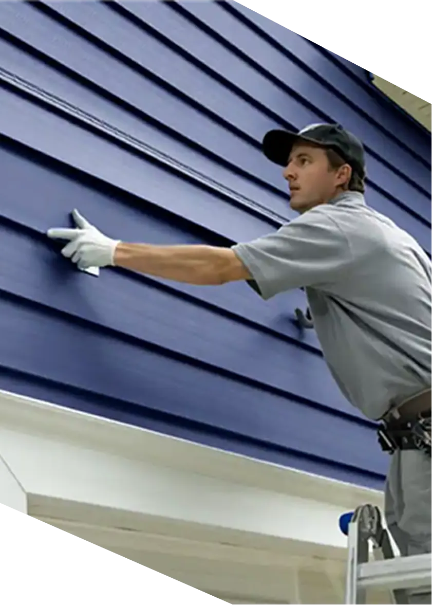 Worker in gloves on ladder installing or inspecting blue house siding panels.