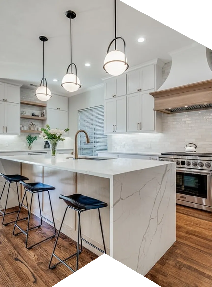 Modern kitchen with white marble island, black bar stools, hanging lights, and stainless steel stove.