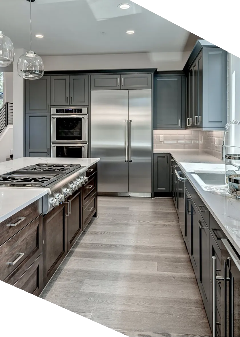 Modern kitchen with gray cabinets, stainless steel refrigerator, double oven, and gas stove on island.