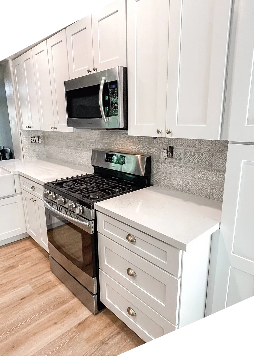 Modern kitchen with white cabinets, stainless steel microwave and stove, patterned backsplash, wood floor.