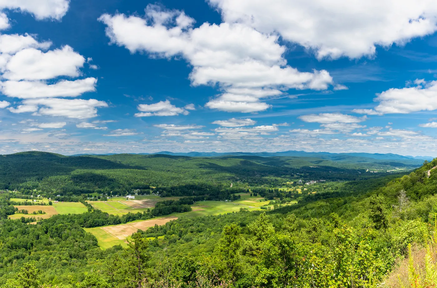 Panoramic view of green hills, fields, and forests under a blue sky with scattered white clouds.