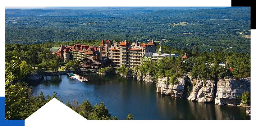 Large historic hotel by a lake surrounded by cliffs and dense forest under a clear sky.
