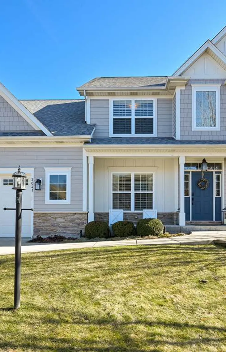 Modern two-story house with blue front door, white shutters, stone accents, and a front lawn.