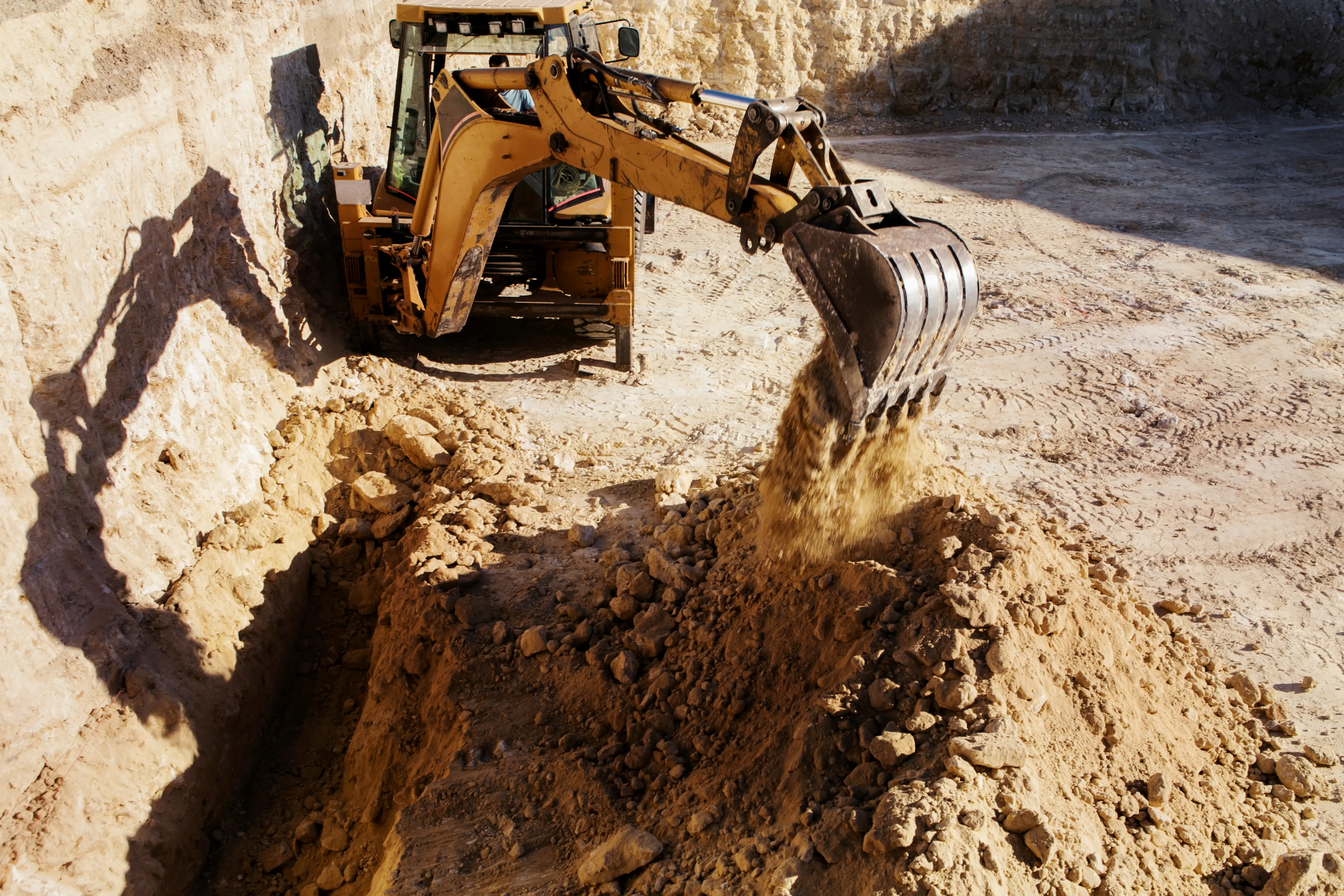 Yellow excavator digging dirt and rocks in a large outdoor construction site during daylight.