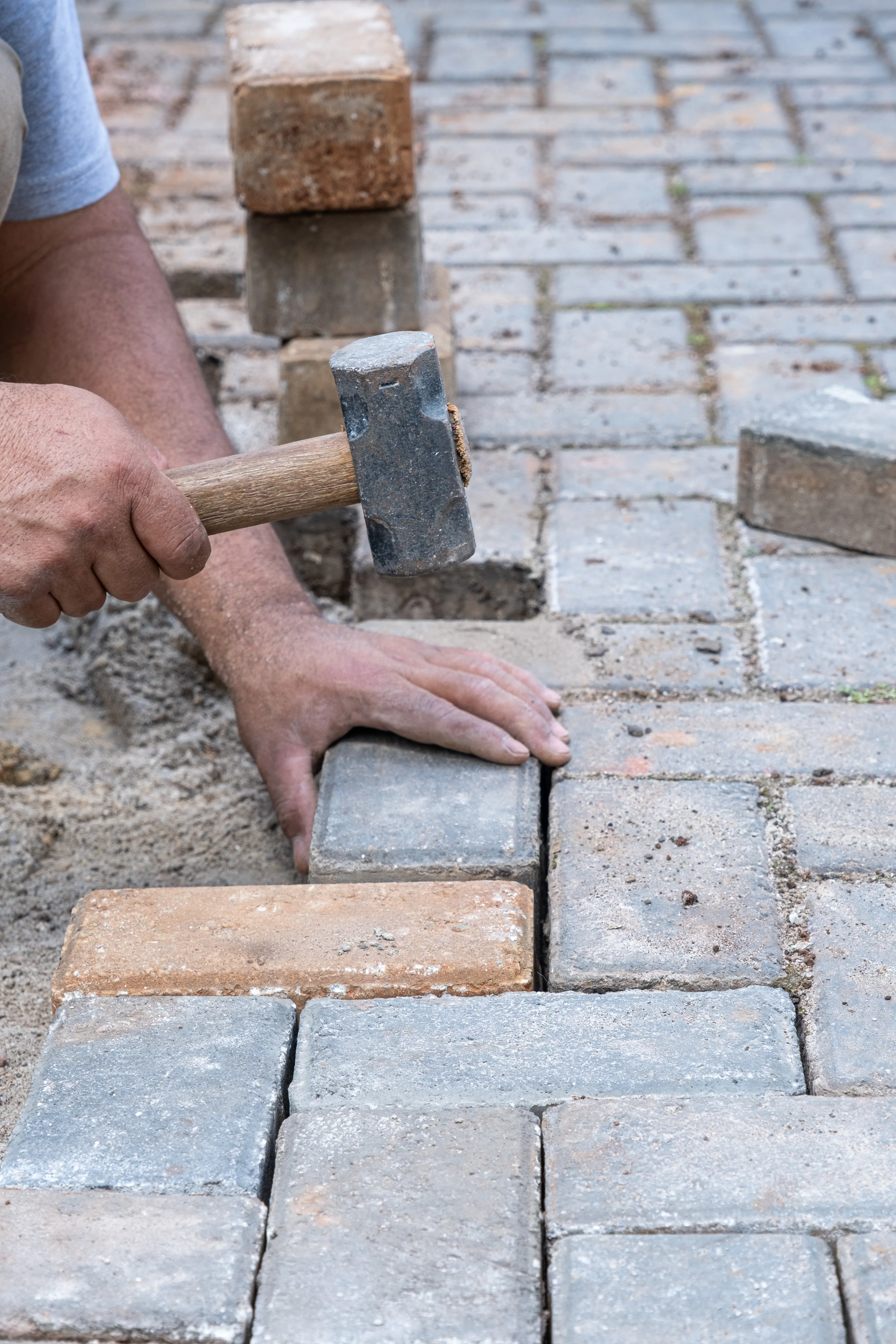 Hands using hammer to fit paving stones into place on a stone pathway under construction.