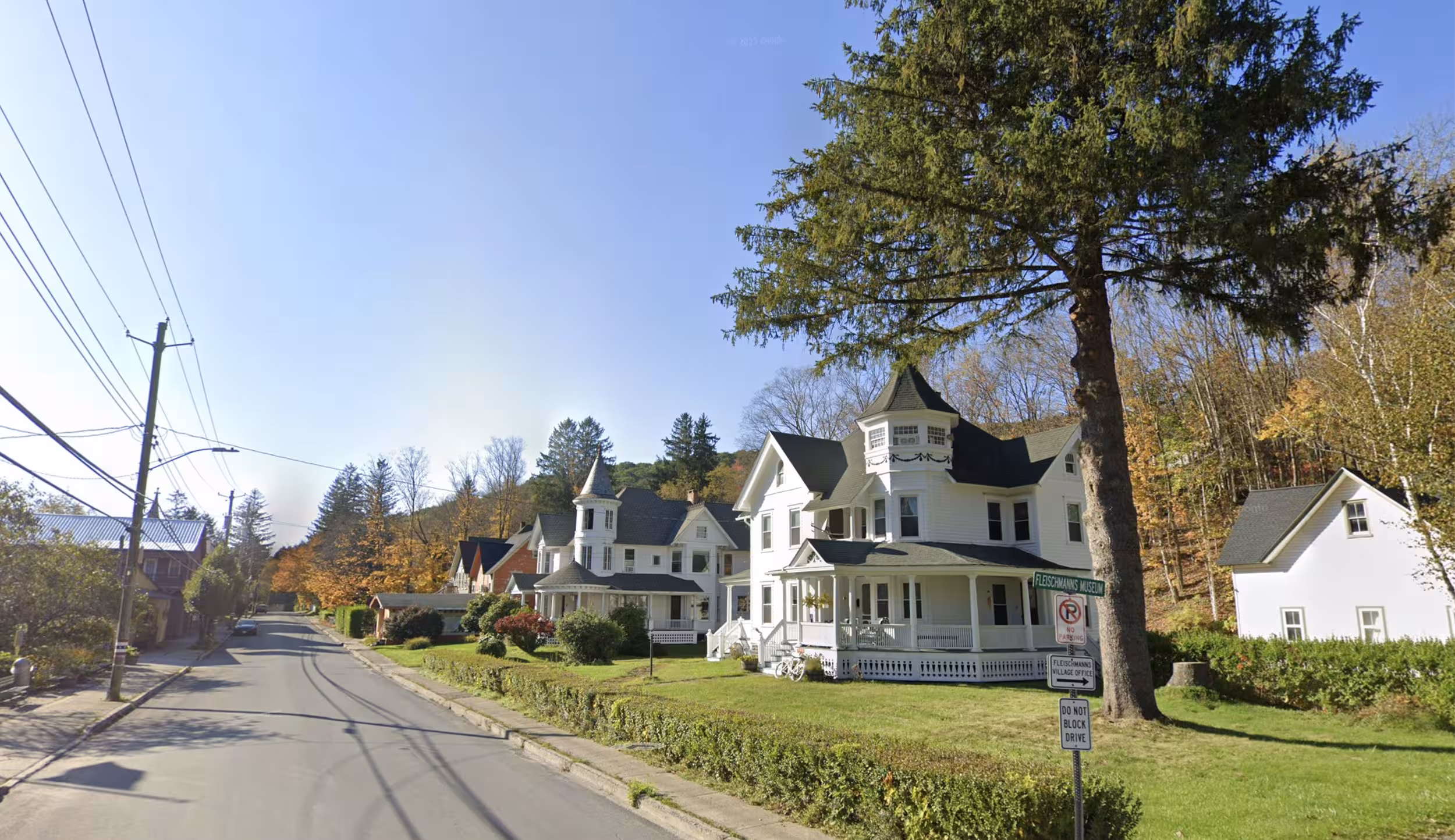 Street view of large white Victorian houses with pointed roofs and a museum sign in a small town.