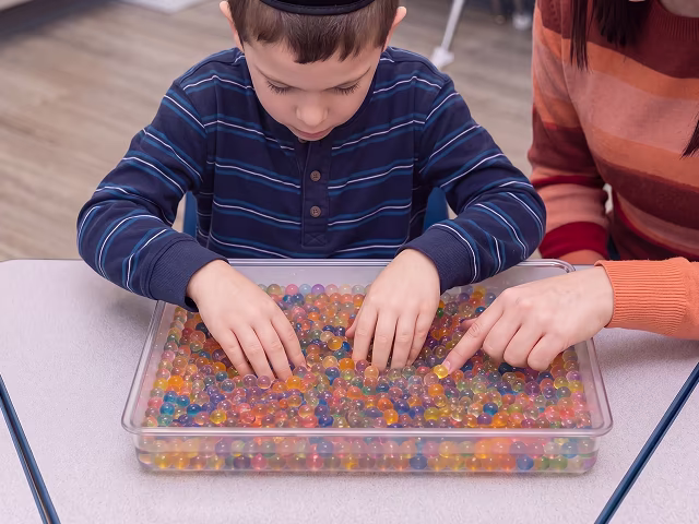Boy playing with colorful water beads in a clear tray.