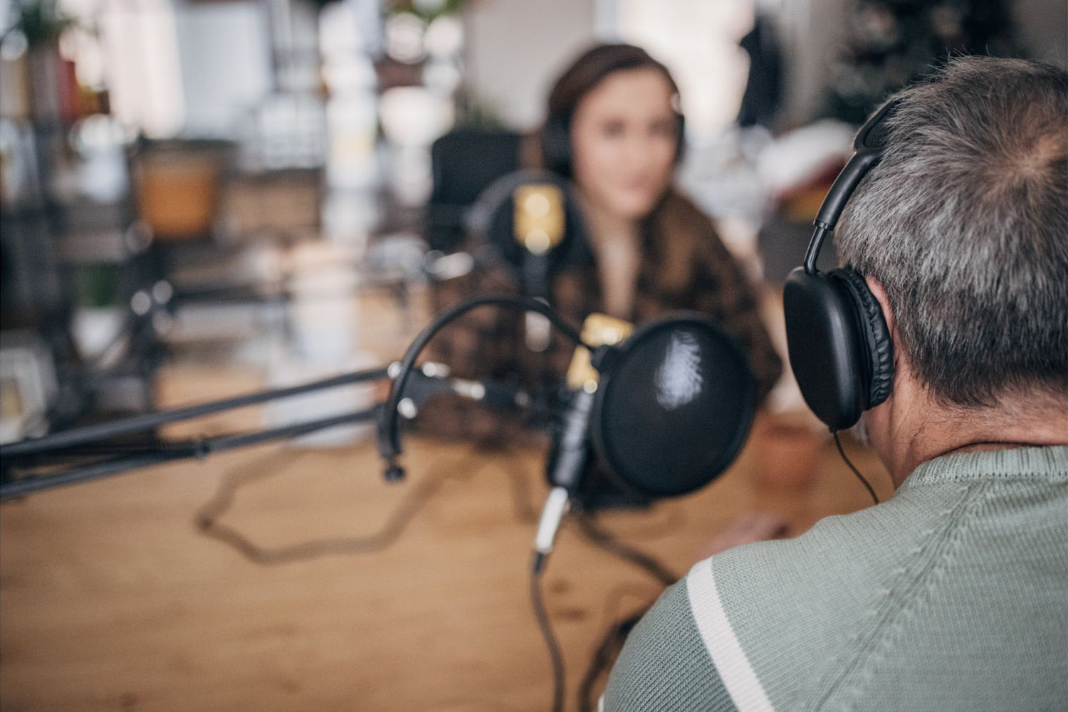 Two people wearing headphones speaking into microphones at a podcast recording table.