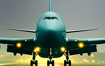 Front view of a large airplane with headlights on the runway at dusk.