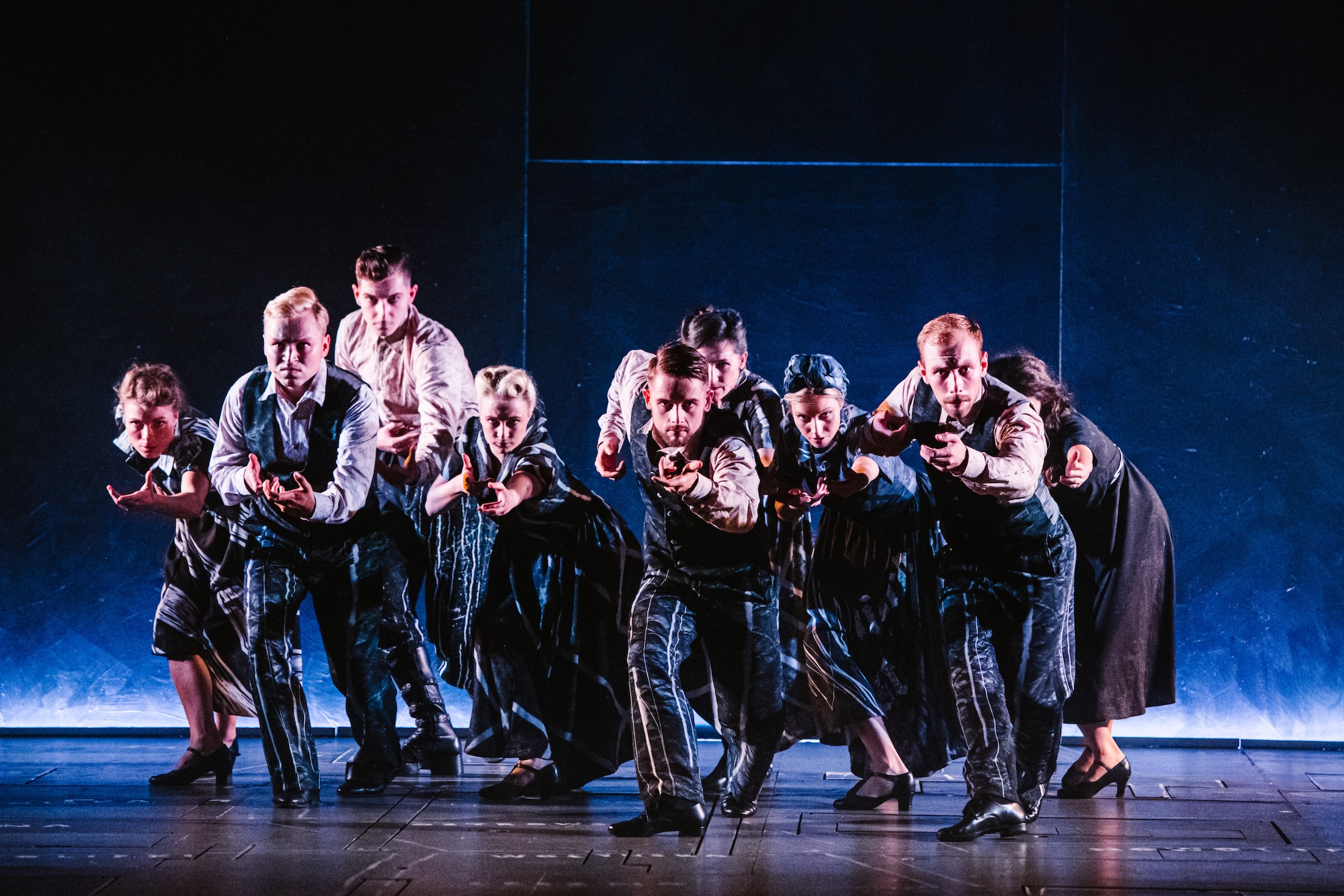 The Irena ensemble advances in formation, holding guns in a tense blue-lit stage moment.