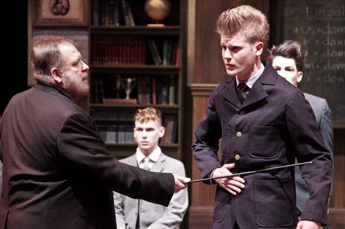 An adult man confronts a young man while other students watch in a classroom scene from Spring Awakening.