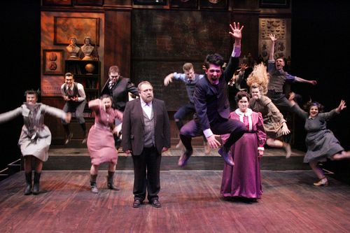 The Spring Awakening ensemble erupts in movement around two rigid adults in a classroom.