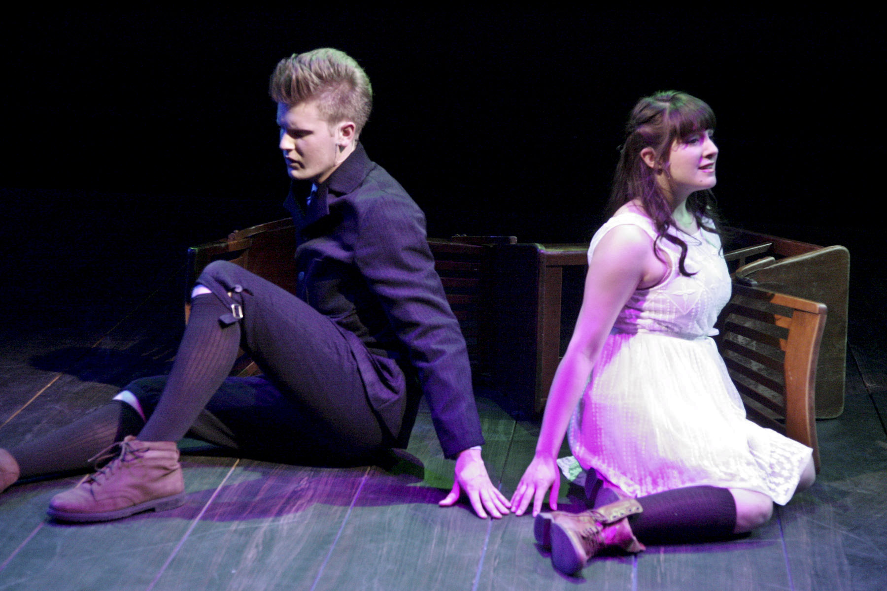 A young man and young woman sit apart on the floor in a quiet scene from Spring Awakening.