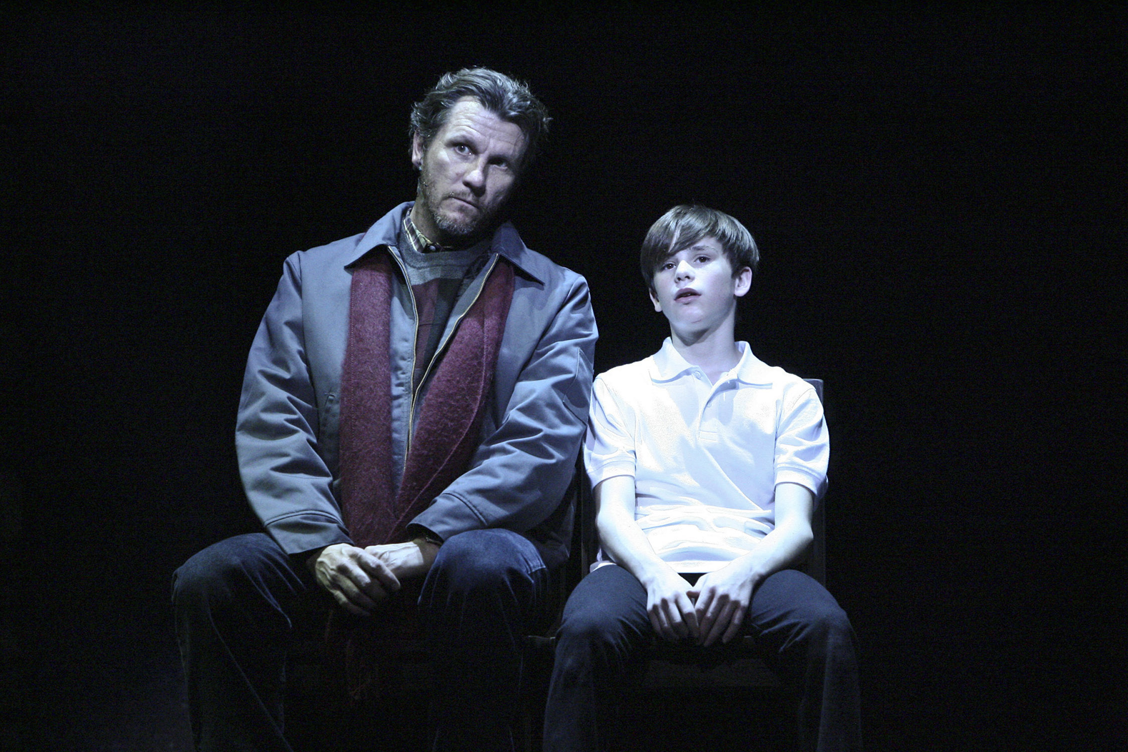 Billy and his father sit side by side under a spotlight in Billy Elliot.