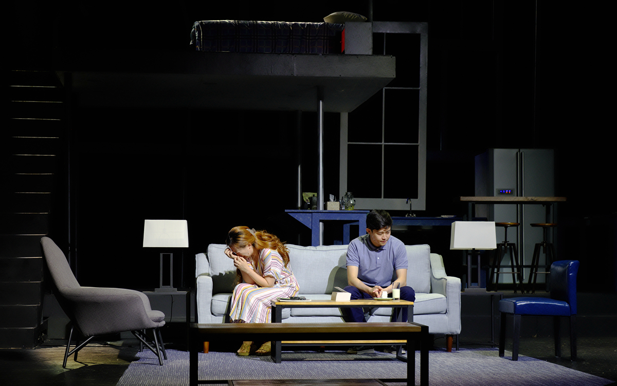 Becca covers her face as Jason sits beside her on a couch in Rabbit Hole.