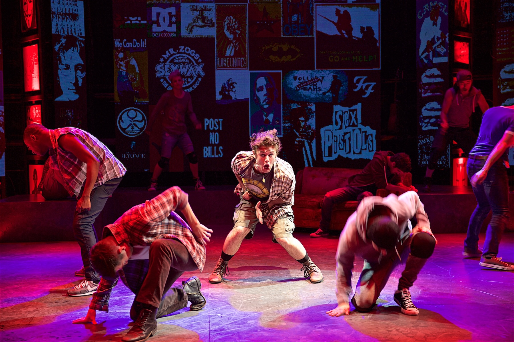The American Idiot ensemble performs the show’s opening number in red stage light.