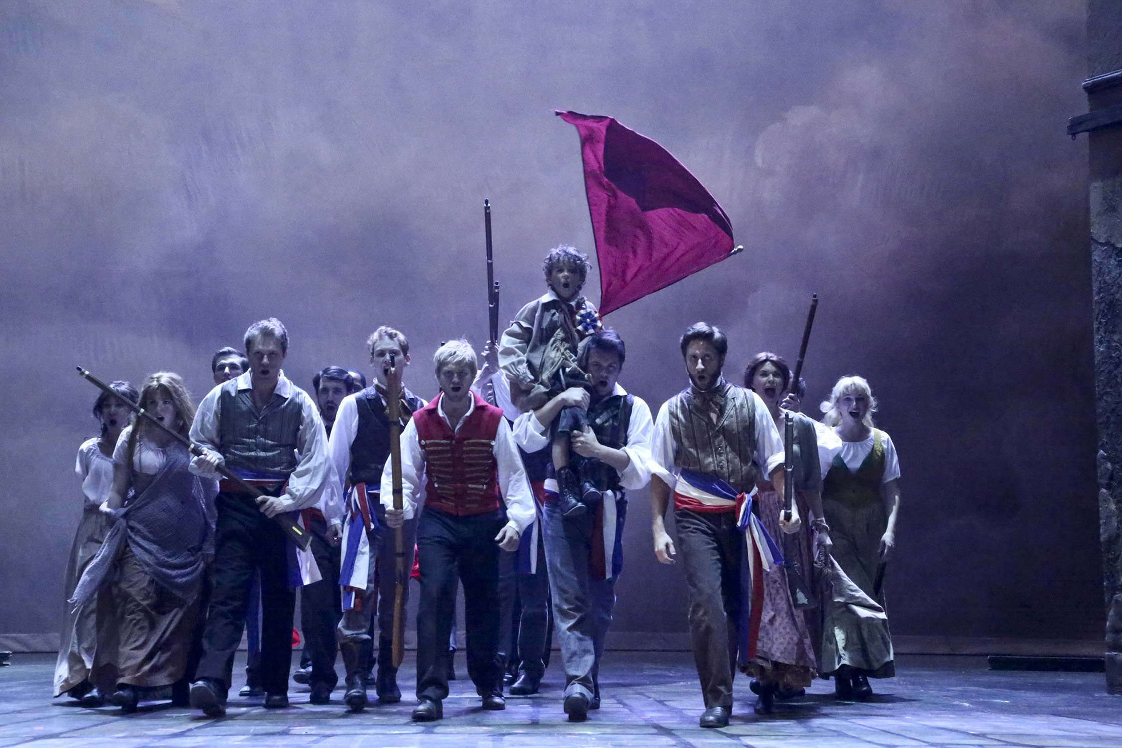 Revolutionaries advance beneath a raised red flag in Les Misérables.
