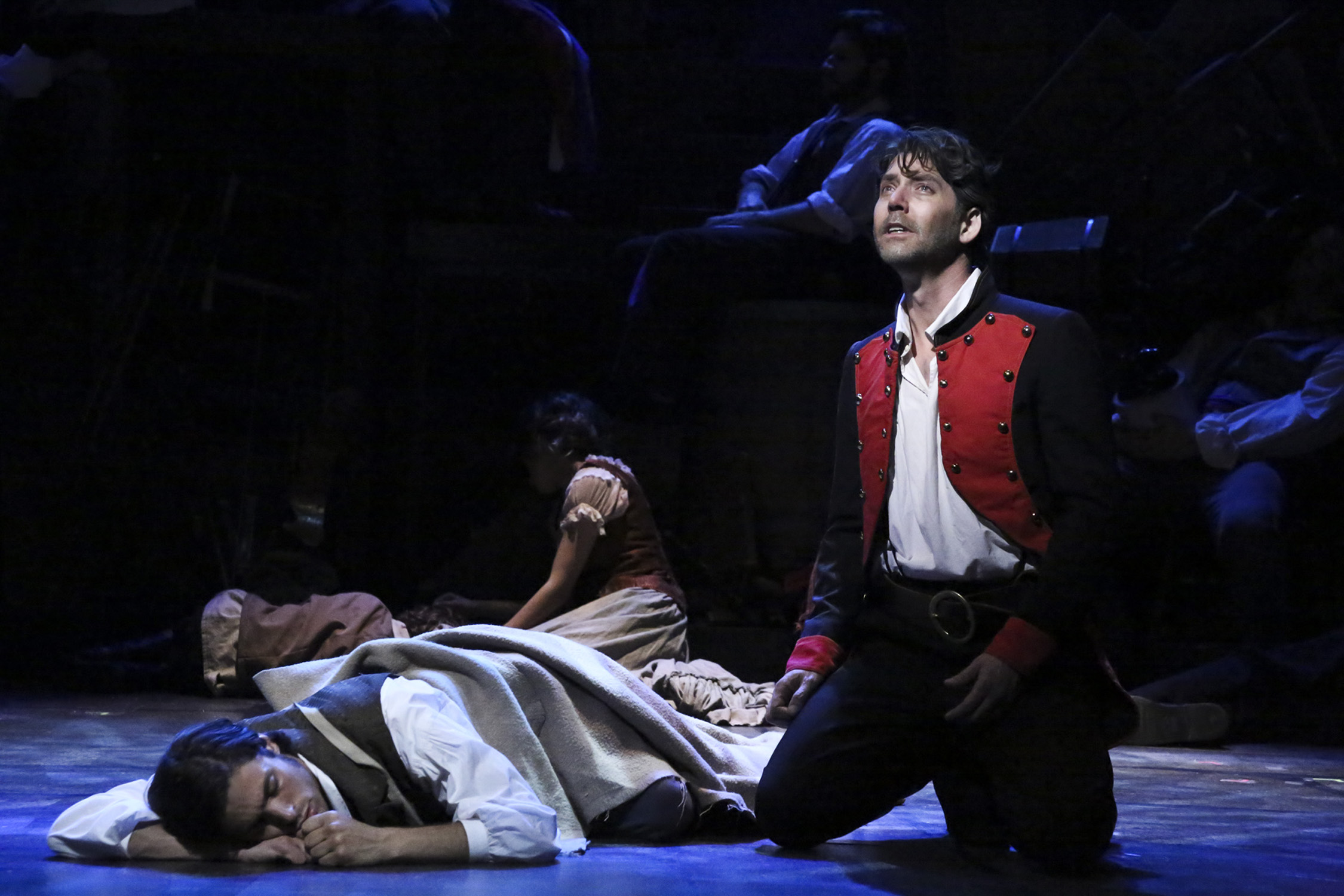 Jean Valjean kneels among fallen bodies at the barricade in Les Misérables.