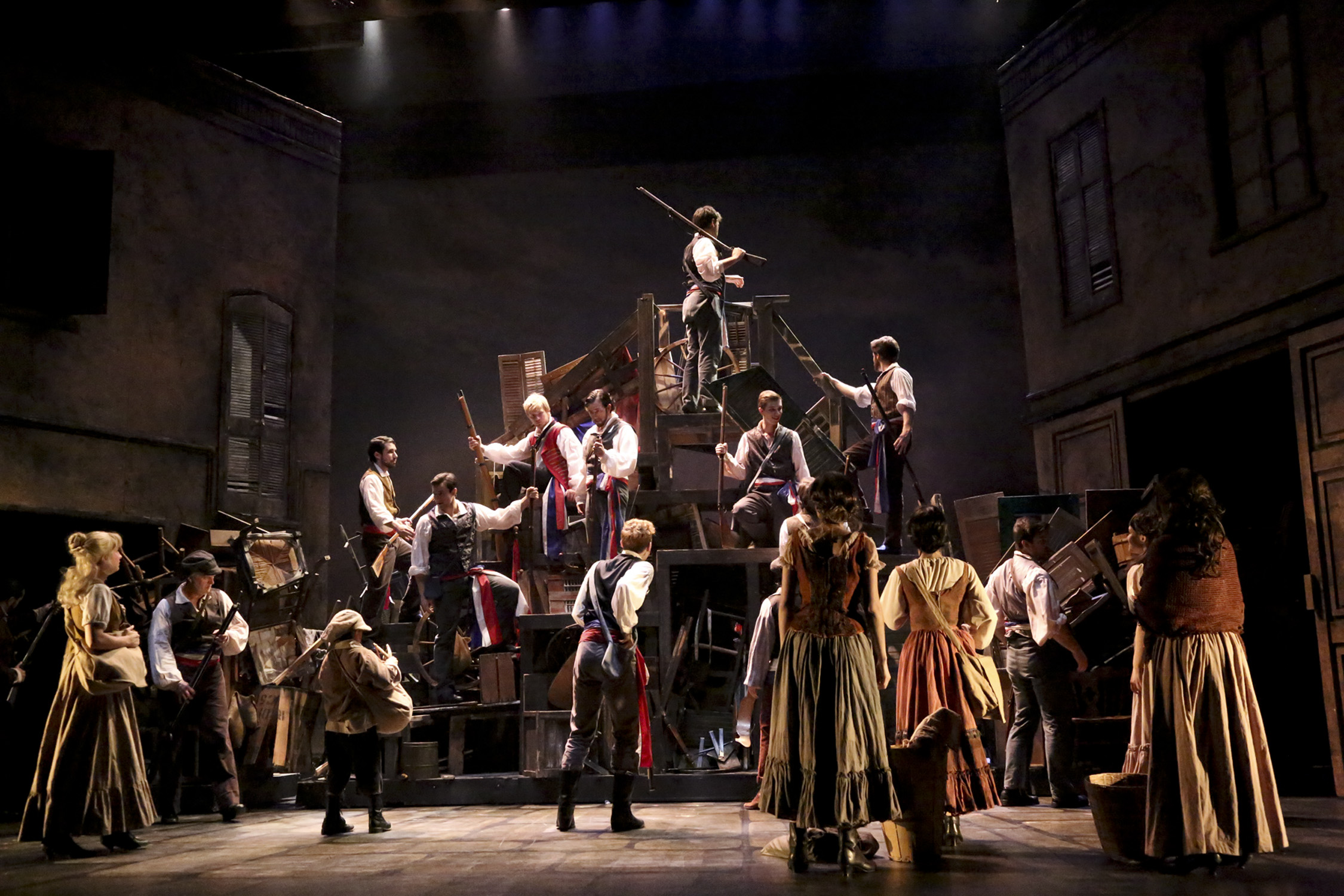 The Les Misérables ensemble gathers around the barricade in a large-scale stage scene.