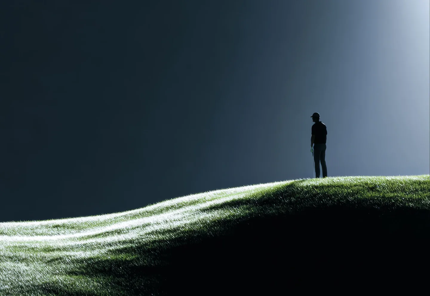 A lone figure standing on a green hill under a shaft of light