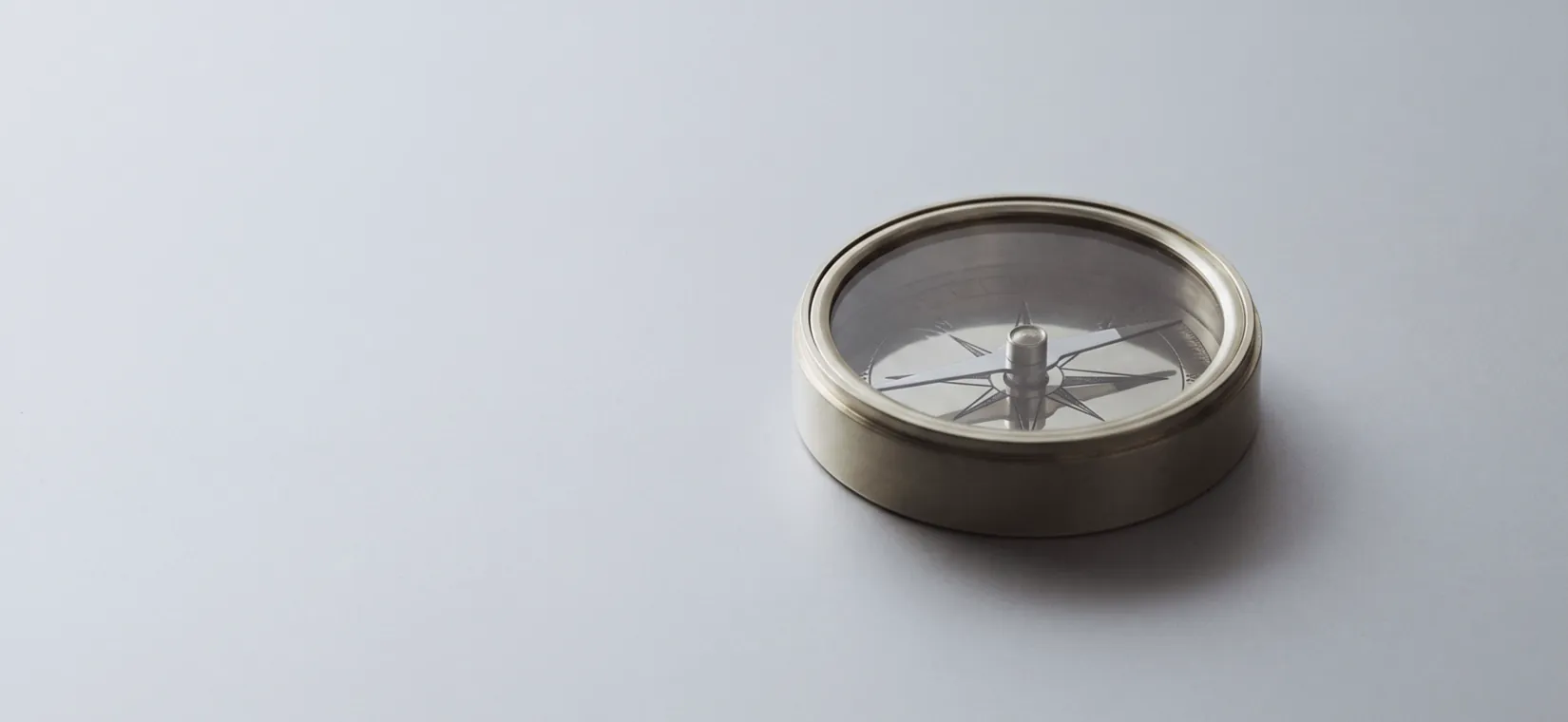 A brass compass resting on a pale grey surface