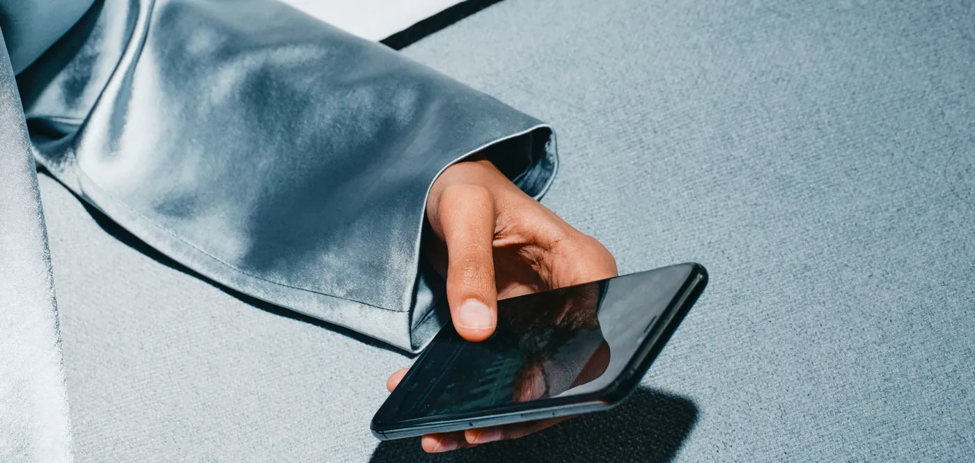 A hand holding a smartphone against a soft grey satin sleeve