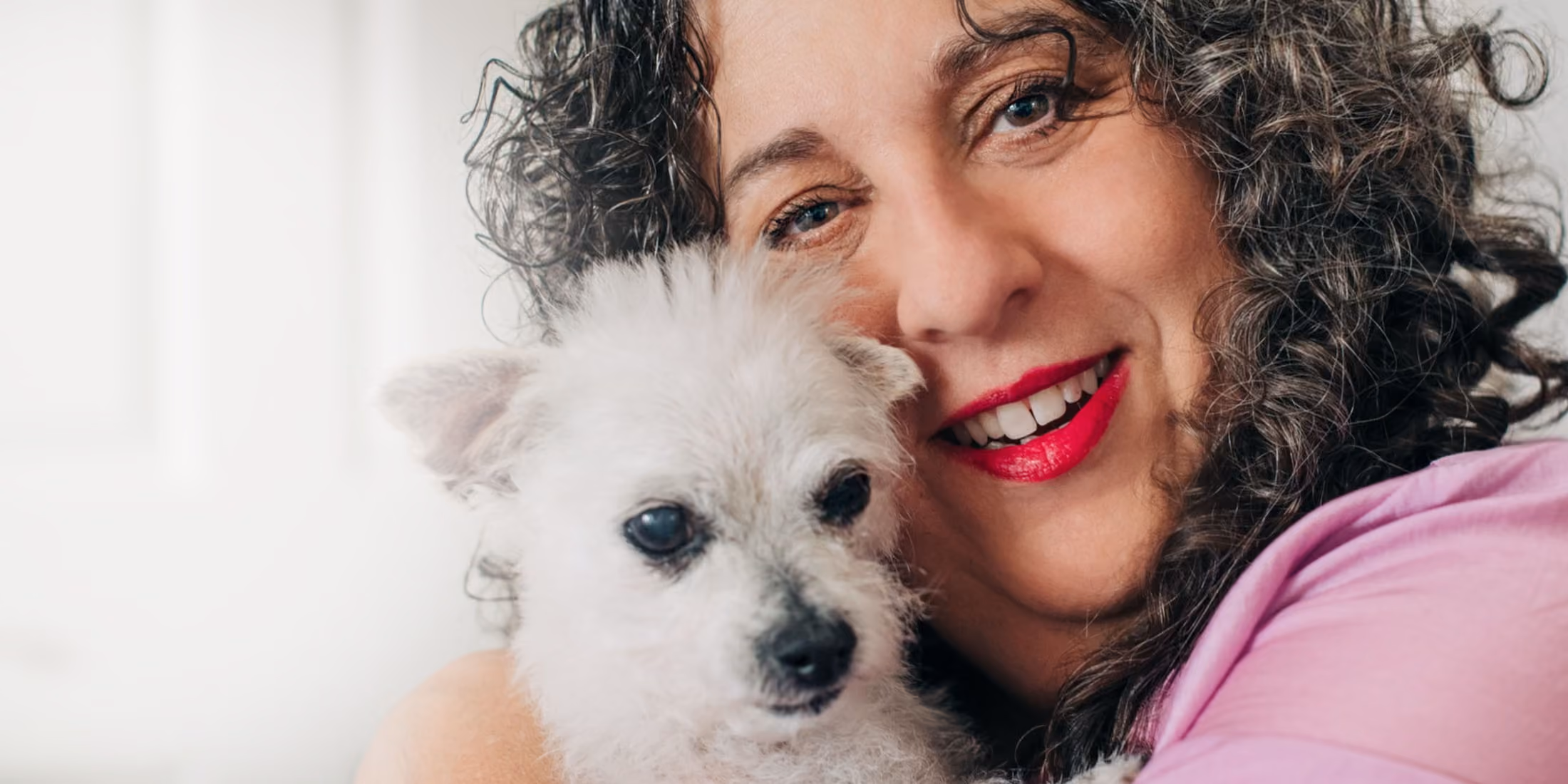 Kara hugging a small white fluffy dog close to her face.