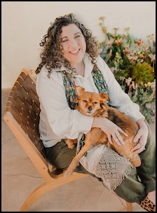 Curly-haired psychic with red dog sits in a chair outdoors