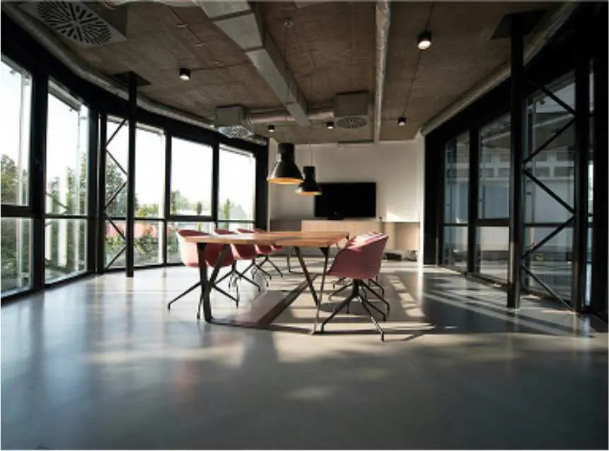 Modern conference room with large windows, six red chairs around a wooden table, black pendant lights, and a wall-mounted TV.