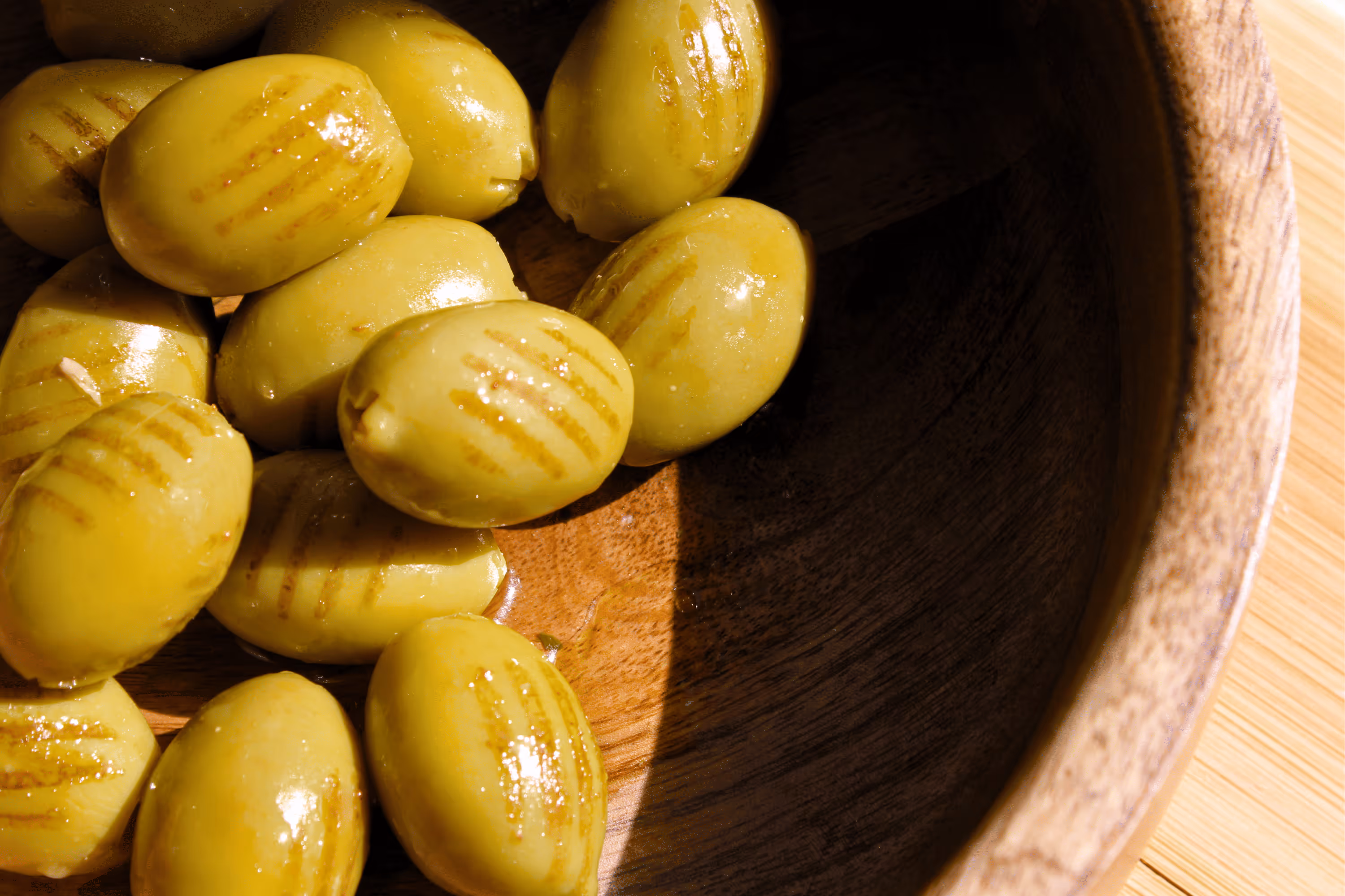Close-up of grilled green olives in a wooden bowl with light reflections.