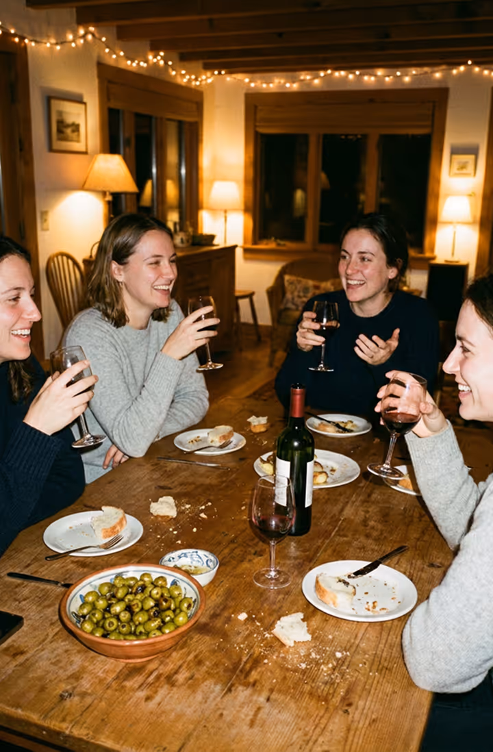 Four women enjoying wine and bread together at a rustic wooden dining table with olives.