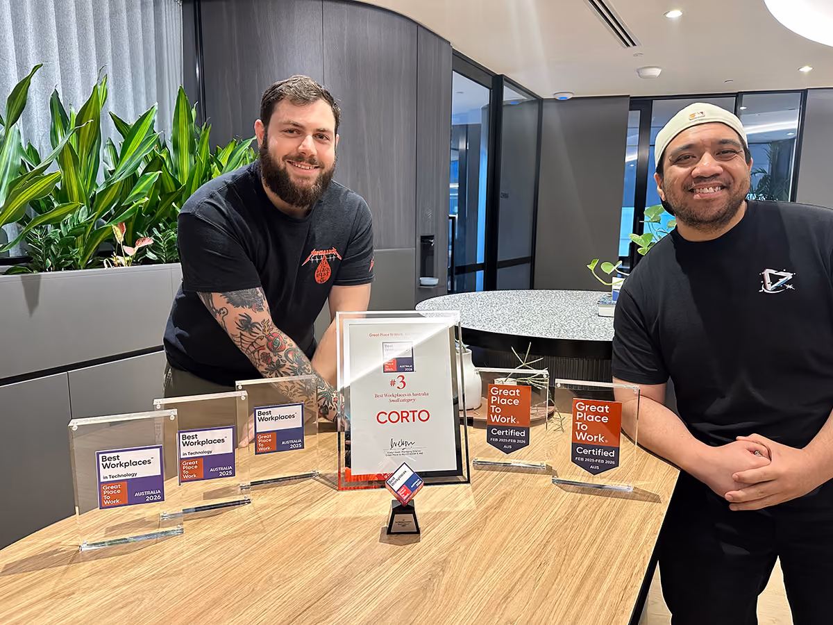 Two employees at the CORTO office in Sydney next to the Great Place to Work awards, including the latest award for 3rd Best Workplace in 2026.