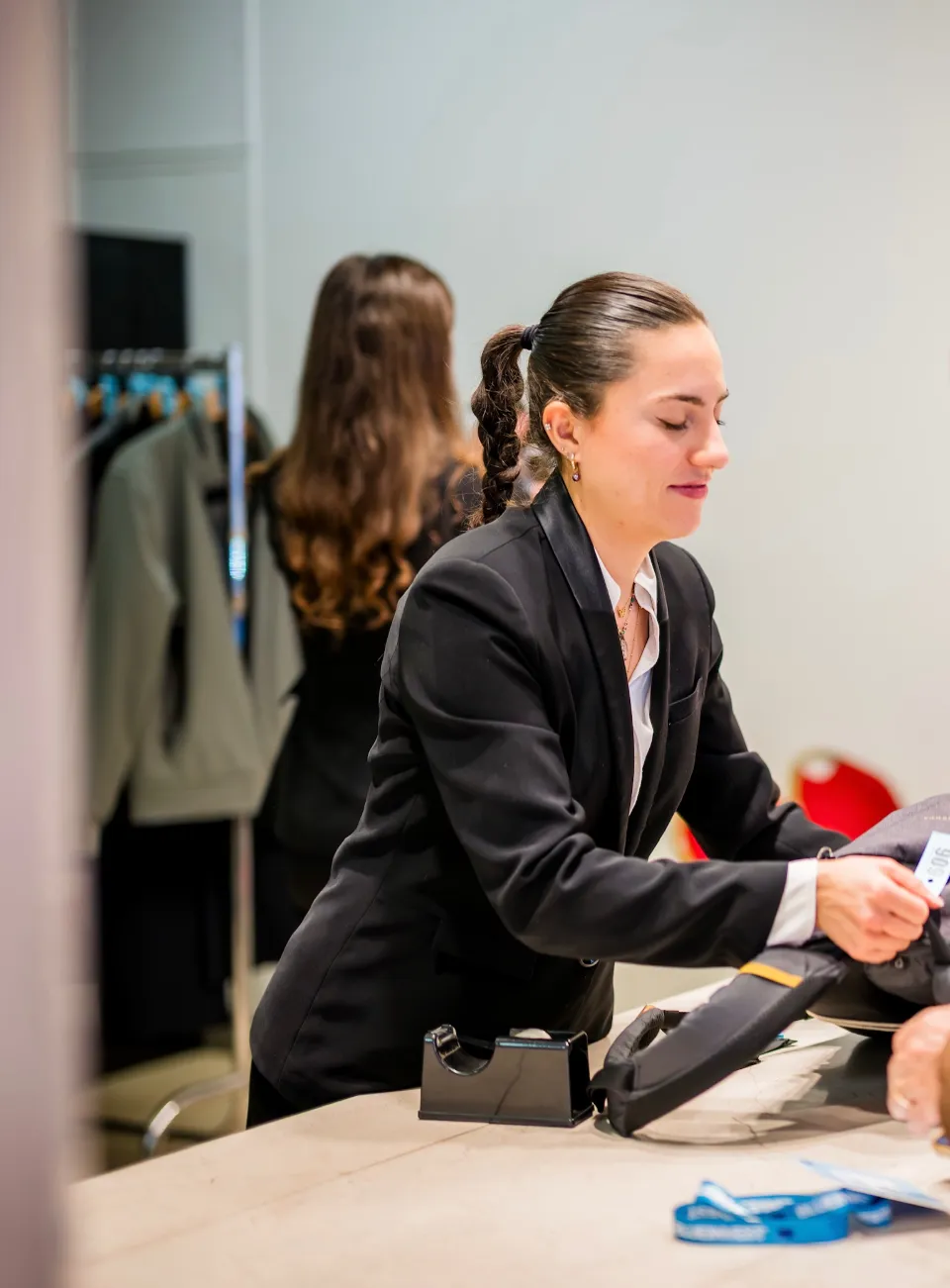 Une travailleuse en veste noire remet un vêtement avec une étiquette de prix dans une boutique.