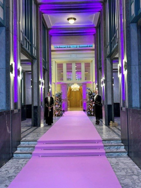 Stewards in Regency costume at the entrance of a Bridgerton-themed evening, pink carpet and purple lighting