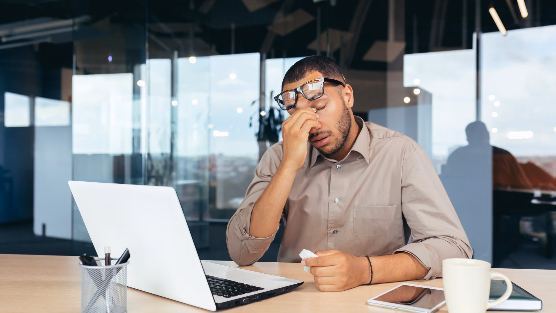 Man rubbing his eyes while working on a laptop, showing digital eye strain and fatigue